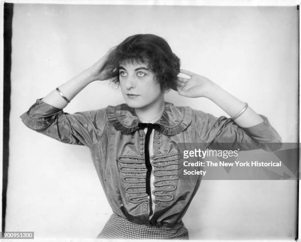 Model in taffeta blouse with ruffled collar and black velvet tie; hands behind head, 1911.