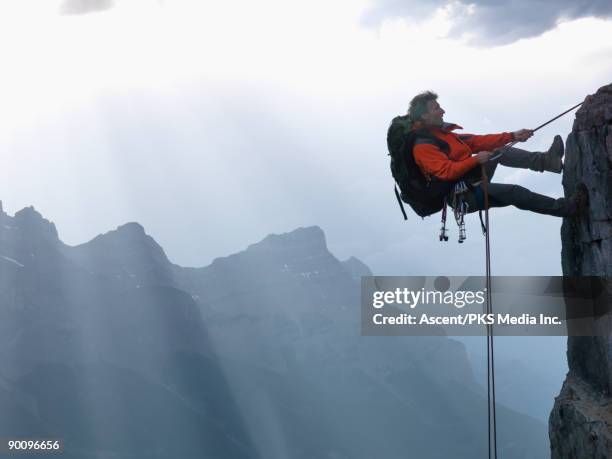 climber rappels (abseils) down cliff, mtns behind - cliff side stock pictures, royalty-free photos & images