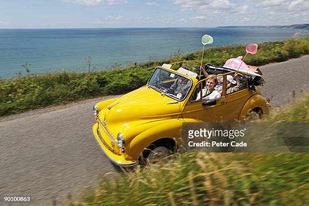 family in open top car on coastal road - yellow car stock pictures, royalty-free photos & images