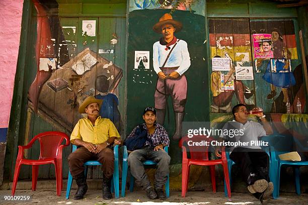 In the main square of Jinotega town people rest, drink or eat at a street snack stop, against a revolutionary mural depicting Agusto Sandino and Che...