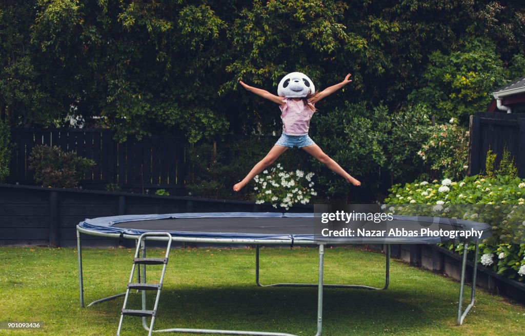 Young girl jumping on trampoline with Panda mask on.