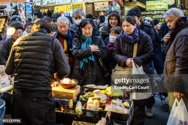 People watch a salesman demonstrate a kitchen implement as he sells his wares in Ameya Yokocho market on January 4, 2018 in Tokyo, Japan. Ameya...