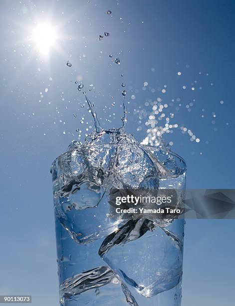 ice cubes and splash water in glass on blue sky - sunlight through drink glass foto e immagini stock