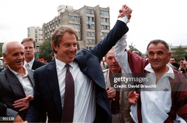 British Prime Minister Tony Blair greets an ethnic Albanian by holding up his hand in central Pristina, Yugoslavia during a one-day visit Saturday...