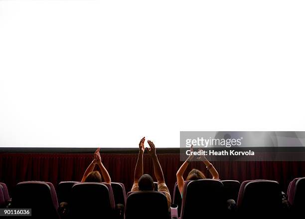 three people clapping at blank screen in theater. - small group of people stock-fotos und bilder