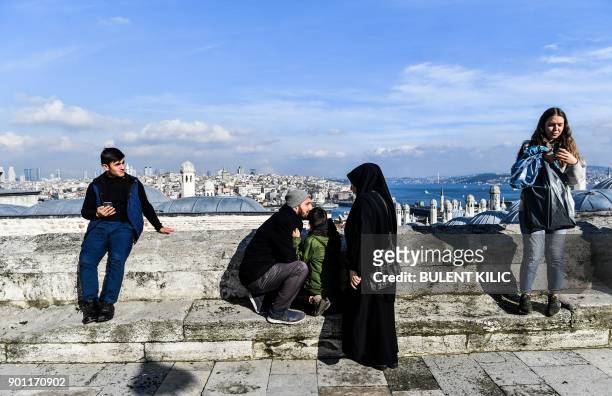 People enjoy the view of The Bosphorus from a terrace of Mimar Sinan Mosque as the sun shines in Istanbul on January 4, 2018. / AFP PHOTO / Bulent...