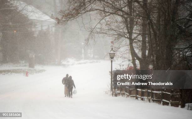 People walk down main st. As a blizzard hits the Northeastern part of the United States January 4, 2018 in Stony Brook, New York.