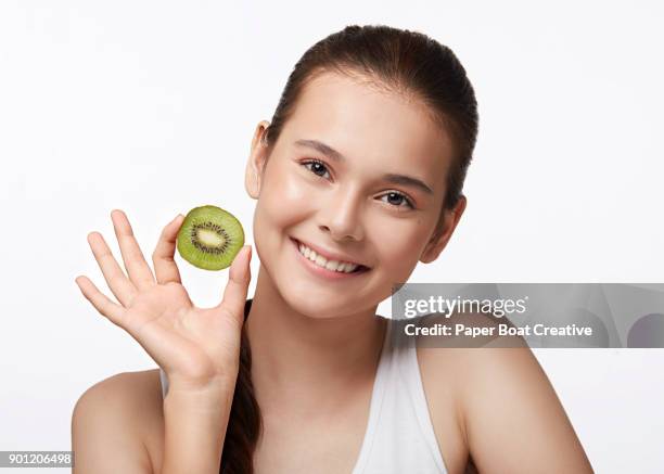 young woman wearing a white tank top, holding a slice of fresh kiwi in her hands, shot in the studio - natural portrait studio shot white background stock-fotos und bilder