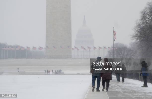People walk alongside a frozen Lincoln Memorial Reflecting Pool on the National Mall during a snow storm in Washington, DC, January 4, 2018. A giant...