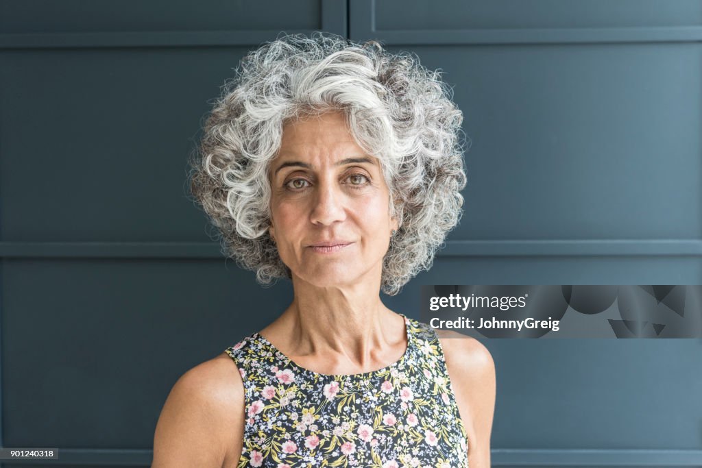 Mature woman with grey curly hair looking at camera