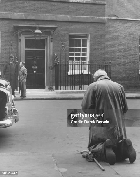 Man kneels in prayer outside Number 10, Downing Street in London, following the announcement of the resignation of Prime Minister Winston Churchill,...