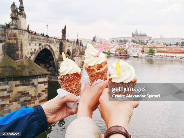 friends eating trdelnik with ice cream with view over charles bridge, prague, czech republic - vltava river stockfoto's en -beelden