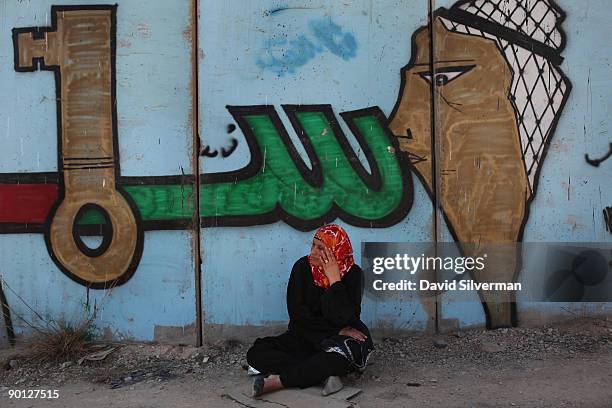 Palestinian woman sits in the shade of Israel's security barrier, which has been covered with Palestinian nationalist graffiti, after being denied...