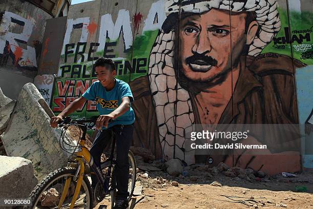 Palestinian boy rides his bicycle beside Israel's security barrier, which has been covered with Palestinian nationalist graffiti, on August 28, 2009...