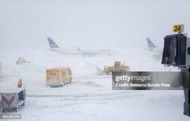 Snow plows move snow as a JetBlue airplane waits outside terminal five at John F. Kennedy International Airport on January 4, 2018 in the Queens...