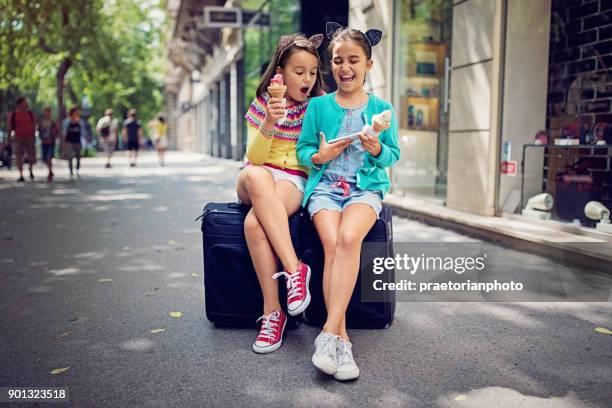 reisenden mädchen auf ihren koffern sitzen und suchen in ihrem handy - freundinnen urlaub sommer eis stock-fotos und bilder
