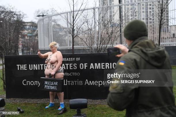 Ukrainian national guard serviceman, guarding the US embassy in Kiev, takes pictures as a topless activist of the Ukrainian women's movement Femen...