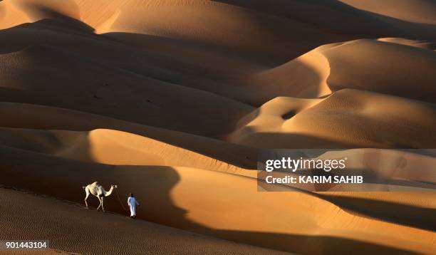 An Emirati man walks with a camel in the Liwa desert, some 250 kilometres west of the Gulf Emirate of Abu Dhabi, during the Liwa 2018 Moreeb Dune...