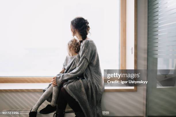 young woman and girl looking out of window - mom and young daughter ストックフォトと画像