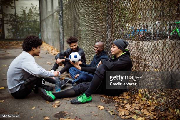 fußball-spieler sprechen beim sitzen gegen zaun - street football stock-fotos und bilder
