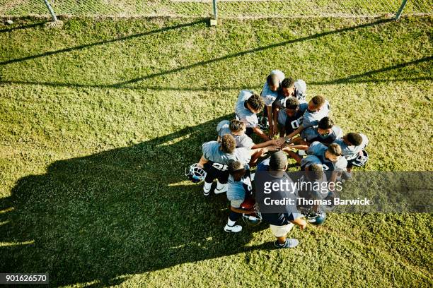 overhead view of coach and football team gathered in circle with hands together before football game - sport di squadra foto e immagini stock