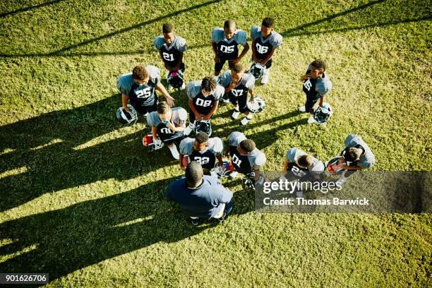 overhead view of football coach talking to young players before football game - footballtrikot stock-fotos und bilder