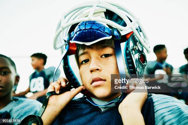 Young football player putting on helmet while sitting with teammates before game