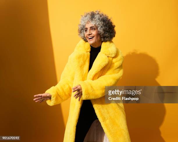portrait of a mature woman dancing and laughing - abrigo amarillo fotografías e imágenes de stock
