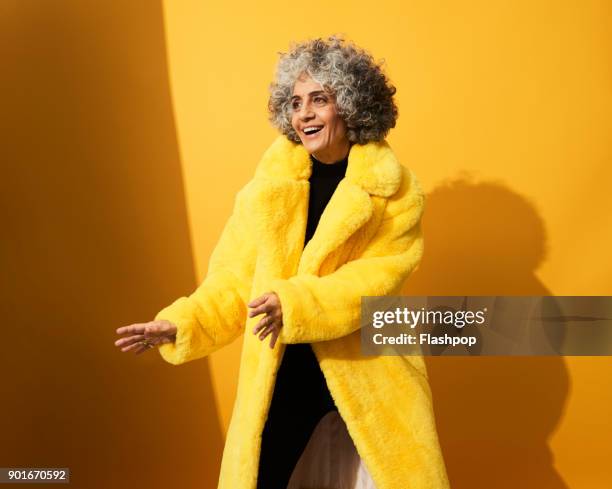 portrait of a mature woman dancing and laughing - yellow coat stock pictures, royalty-free photos & images