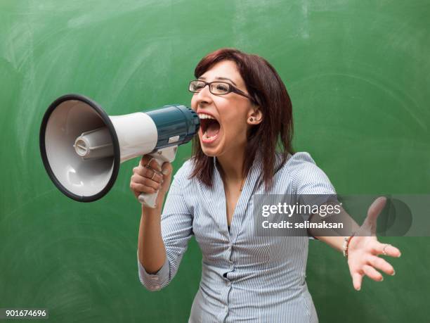 adult woman shouting through megaphone in front of green chalkboard - teacher shouting stock pictures, royalty-free photos & images