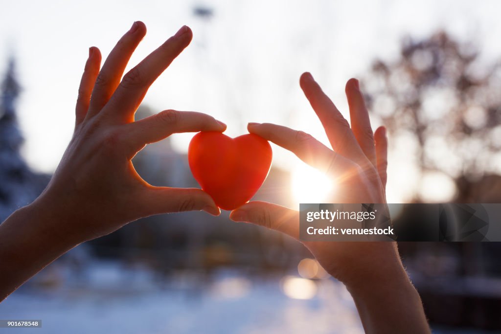 Mains de femme tenant coeur rouge au coucher du soleil