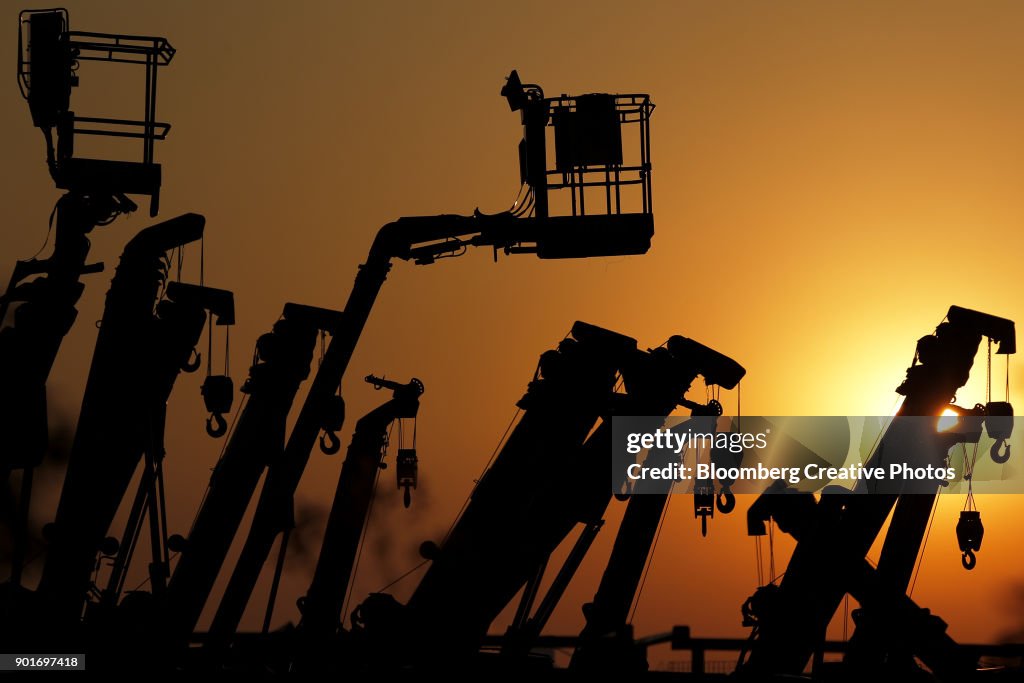 Cranes and boom lifts stand at an equipment rental company
