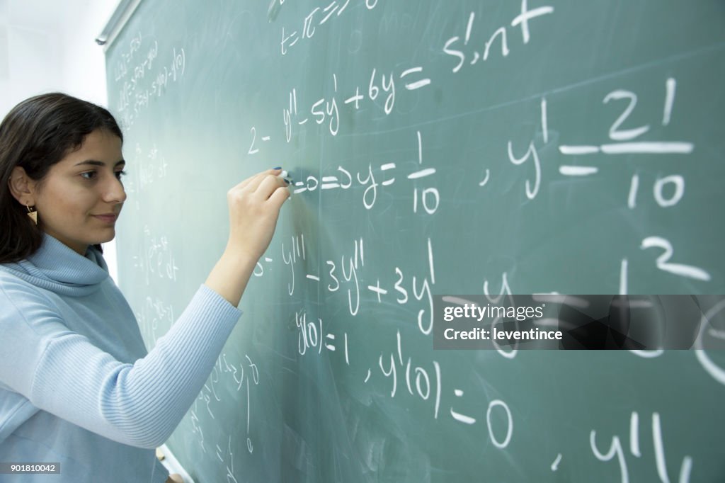 Kvinnlig Student skriver matematisk formel framför svarta tavlan