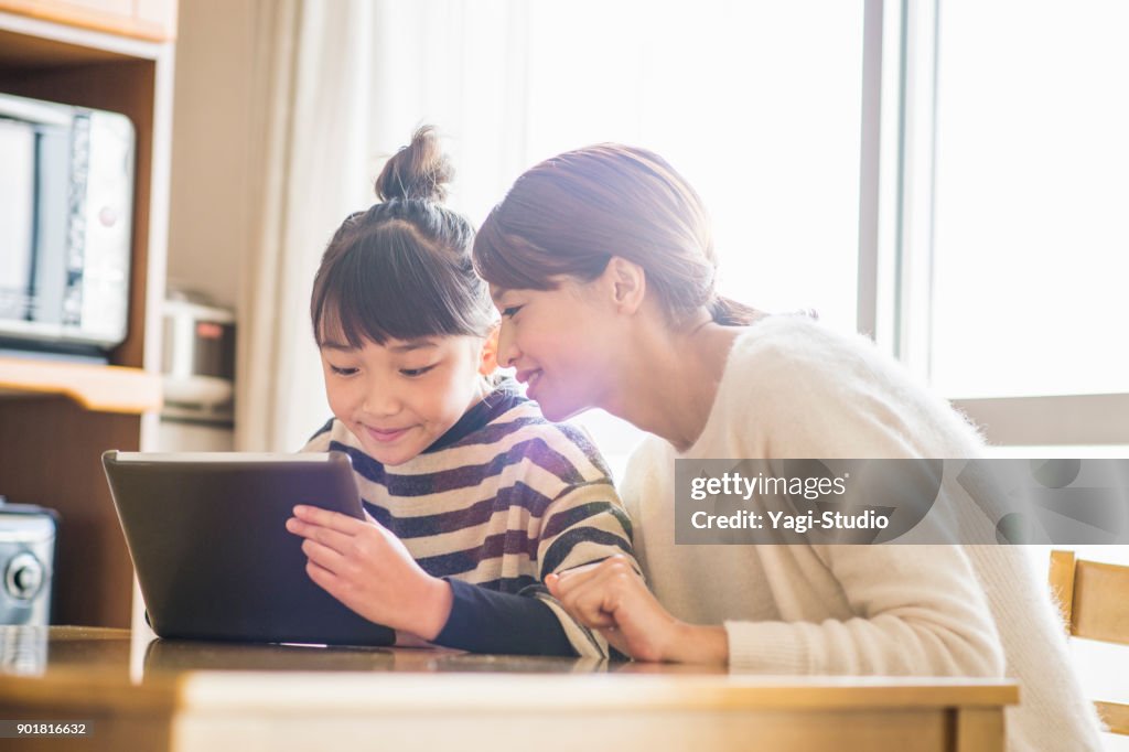 Mother and daughter playing with a digital tablet in room