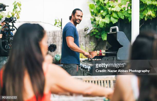 father looking at family while preparing barbecue for them. - new zealand culture stock pictures, royalty-free photos & images
