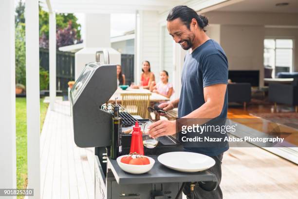 man with smile on his face preparing barbecue for family. - auckland food stock pictures, royalty-free photos & images
