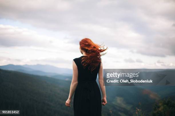 donna in abito nero che cammina in montagna e guarda la vista - vista posteriore foto e immagini stock