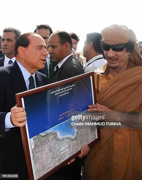 Libyan leader Moamer Kadhafi and Italian Prime Minister Silvio Berlusconi hold a framed map of a highway project during a ceremony to lay its...