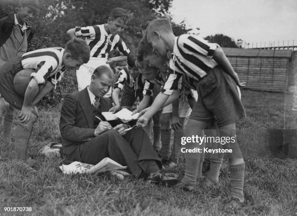 Arsenal footballer Clifford Bastin signs autographs for local boys during a holiday in Exeter, Devon, circa 1935.