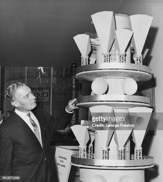 British Conservative politician Reginald Bevins , the Postmaster General, inspects an enlarged model of the Aerial Galleries of the Post Office...