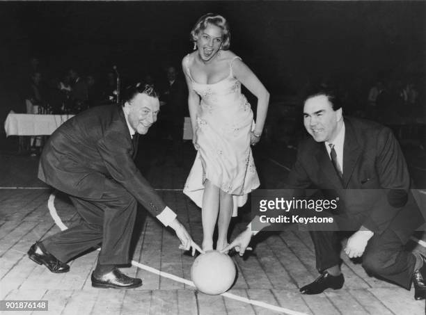 German actress Hannelore Bollmann prepares to kick a ball into an empty barrel, assisted by actor Willy Fritsch and former heavyweight boxing...