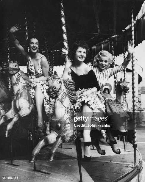 From left to right, actresses Angela Lane, Barbara Roscoe and June Cunningham take a ride on the merry-go-round at the Battersea Fun Fair in London,...