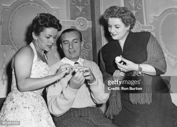 From left to right, singer Eve Boswell , golfer Henry Cotton and singer Anne Shelton examine golf balls during a break in rehearsals at the London...