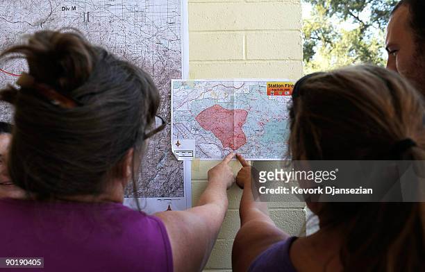 Evacuated resident of Altadena, California, Cecilia Miller and Teresa Martinez look at a map of the Station Fire posted on a wall at an evacuation...