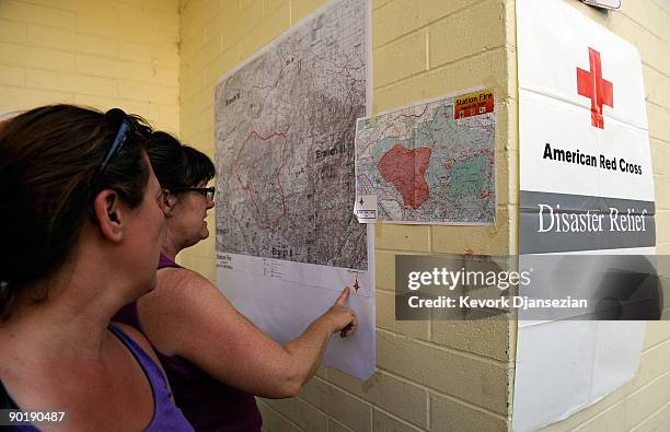 Evacuated resident of Altadena, California, Cecilia Miller and Teresa Martinez look at a map of the Station Fire posted on a wall at an evacuation...