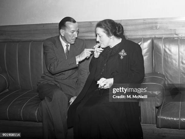 English writer, actor and director Noël Coward lights a cigarette for actress Eva Moore at the Saville Theatre in London, during the AGM of the...