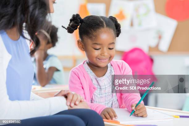 little girl enjoys coloring beside day care worker - differential focus stock pictures, royalty-free photos & images