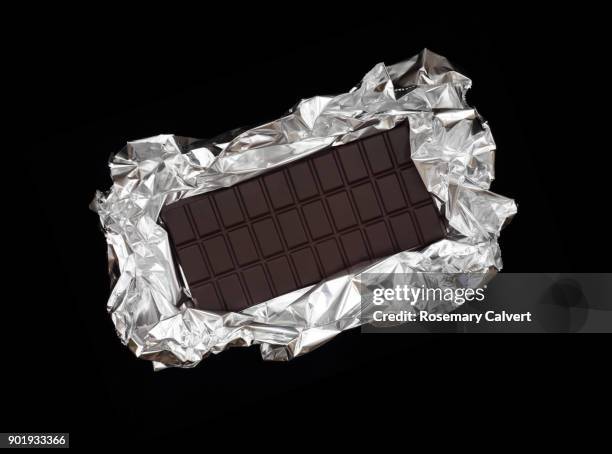 dark chocolate bar on silver foil, black background. - chocolate foil stock-fotos und bilder