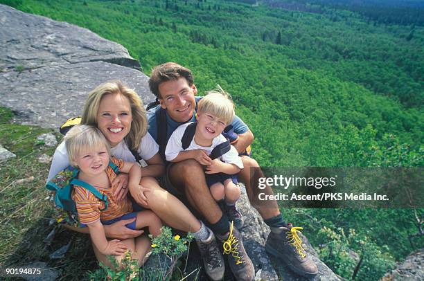 family of hikers look at camera, forest below - front view portrait of four children sitting on rock stock pictures, royalty-free photos & images