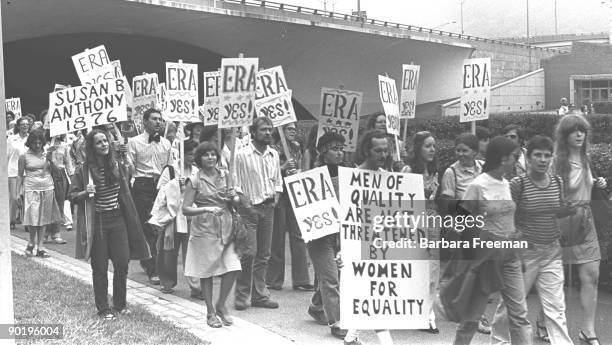 Group of men and women march together holding signs while participating in an ERA protest in Pittsburgh, PA, 1976.